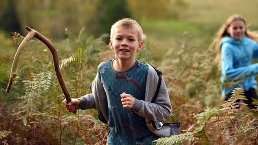 A boy running through woodland at Sutton Hoo holding a long stick
